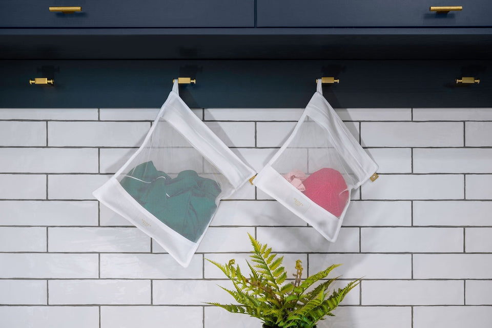 two Hayden Hill white mesh laundry bags hanging on hooks in a tiled laundry room