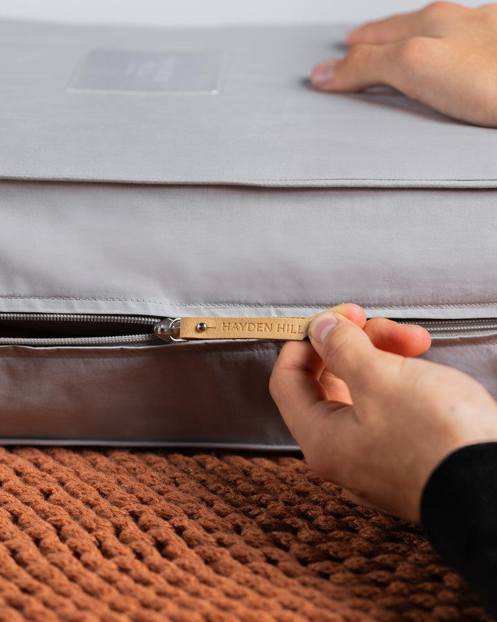 a side view of a grey storage bag being unzipped, showing the Hayden Hill leather zipper pull