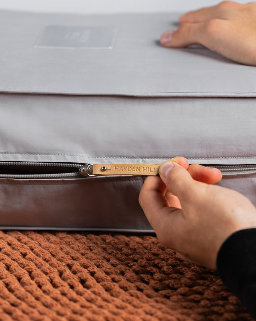 a side view of a grey storage bag being unzipped, showing the Hayden Hill leather zipper pull