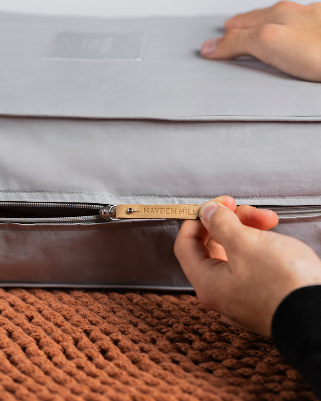a side view of a grey storage bag being unzipped, showing the Hayden Hill leather zipper pull