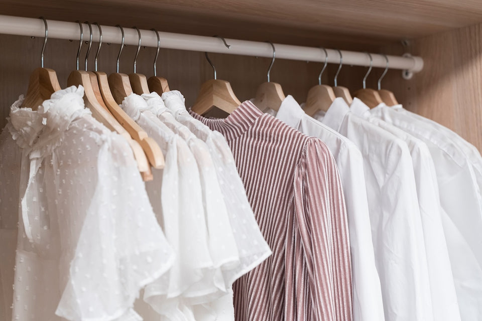 a row of shirts and tops hanging on a rail in a wardrobe