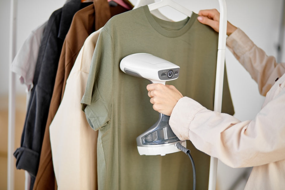 a close up of a handheld steamer being used on a rail of clothes