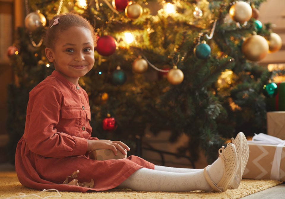 a little girl in her festive party dress sitting by a decorated tree