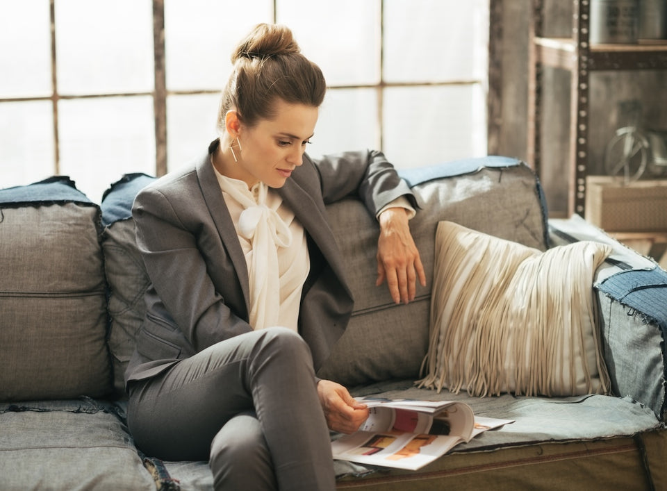 a woman, seated on a sofa,  wearing a tailored jacket and pussybow shirt with smart trousers