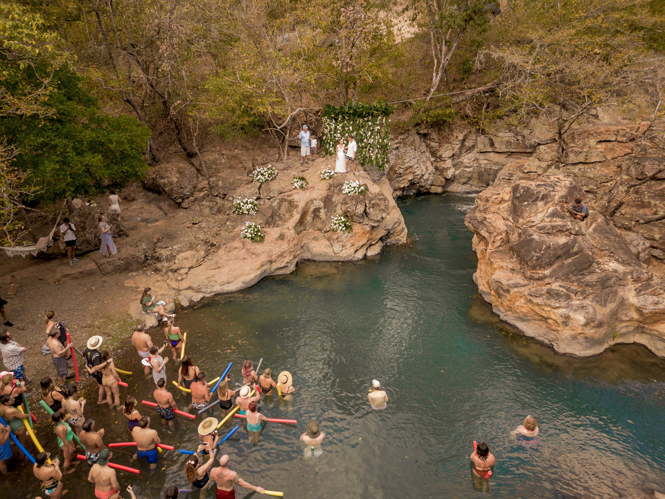 an aerial shot of a wedding ceremony under a waterfall in Costa Rica with the guests watching from the plunge pool below