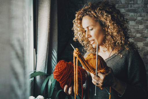 a woman with her knitting which includes two balls of pure wool