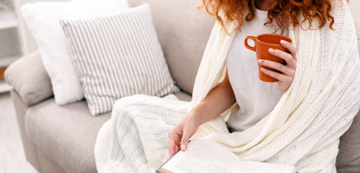 a woman in a cream wool blanket with a cup of coffee