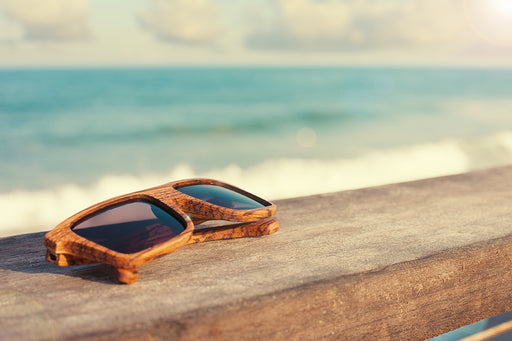 wooden sunglasses placed on a wooden fence with the ocean in the background